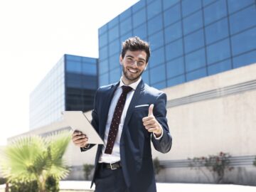 homem de terno na frente de empresas fazendo "joinha" com uma mão